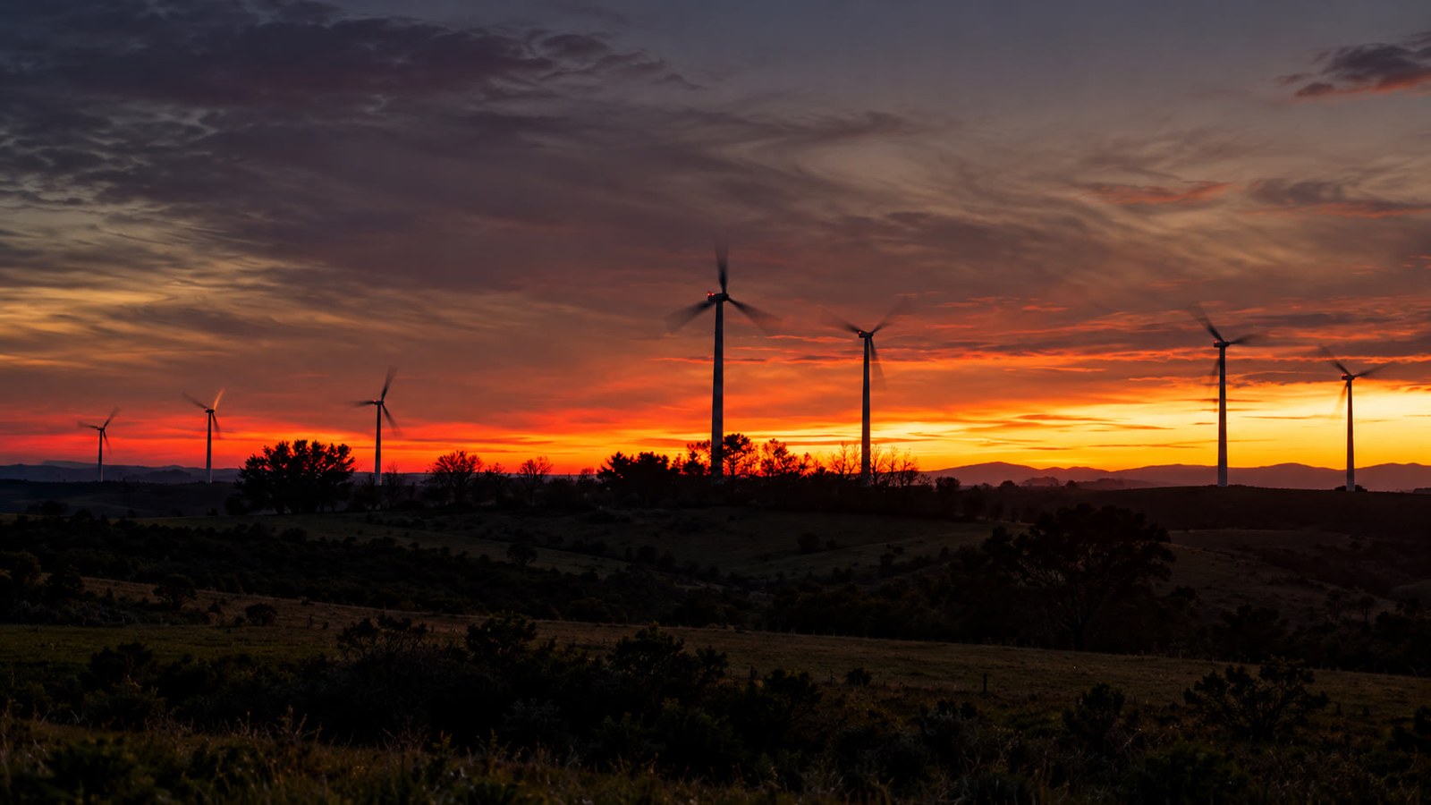 Fotografia ilustrativa de turbinas eólicas em paisagem rural ao entardecer.